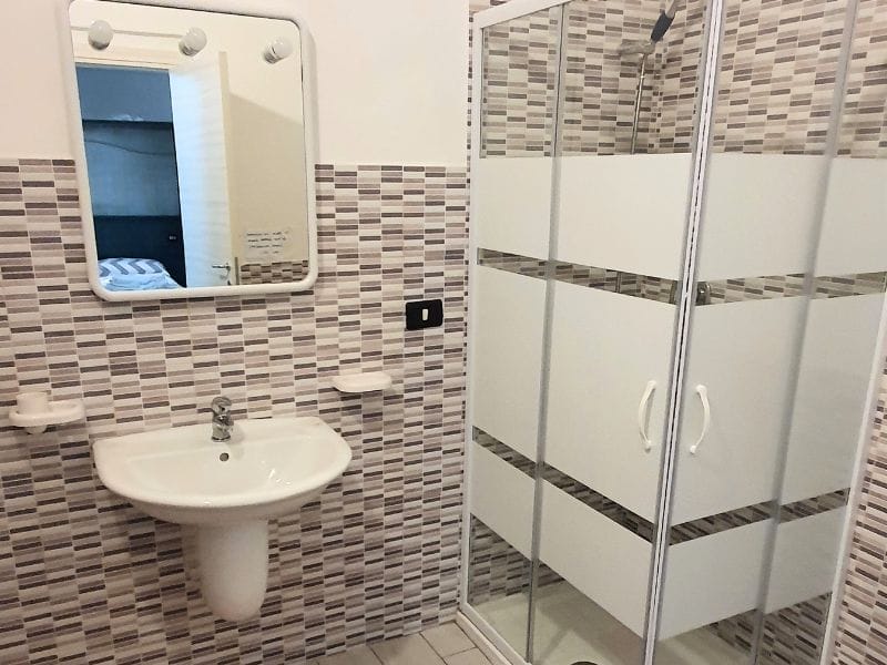 Un bagno con pareti piastrellate, lavabo e doccia in un residence a Lampedusa proposto in affitto per case vacanze.