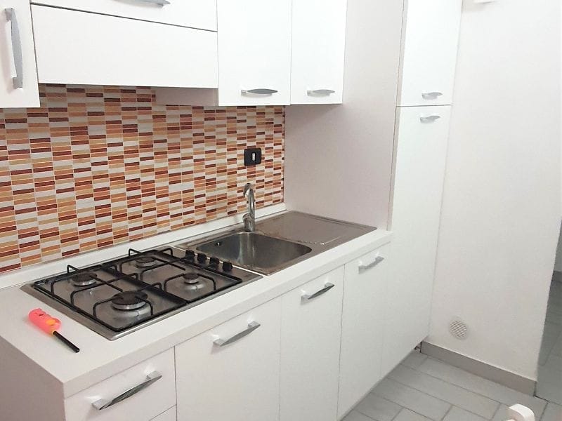 Una piccola cucina con pensili bianchi e piano cottura in un residence a Lampedusa.
