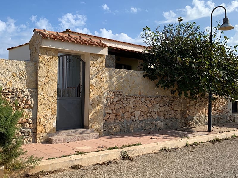 Una casa con un muro in pietra e un albero davanti, perfetta per il tuo soggiorno vacanza a Lampedusa.