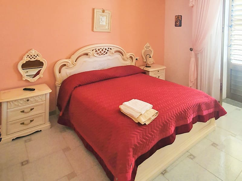 Un letto accogliente con una vivace coperta rossa, perfetto per il relax nelle nostre affascinanti case vacanze a Lampedusa.
