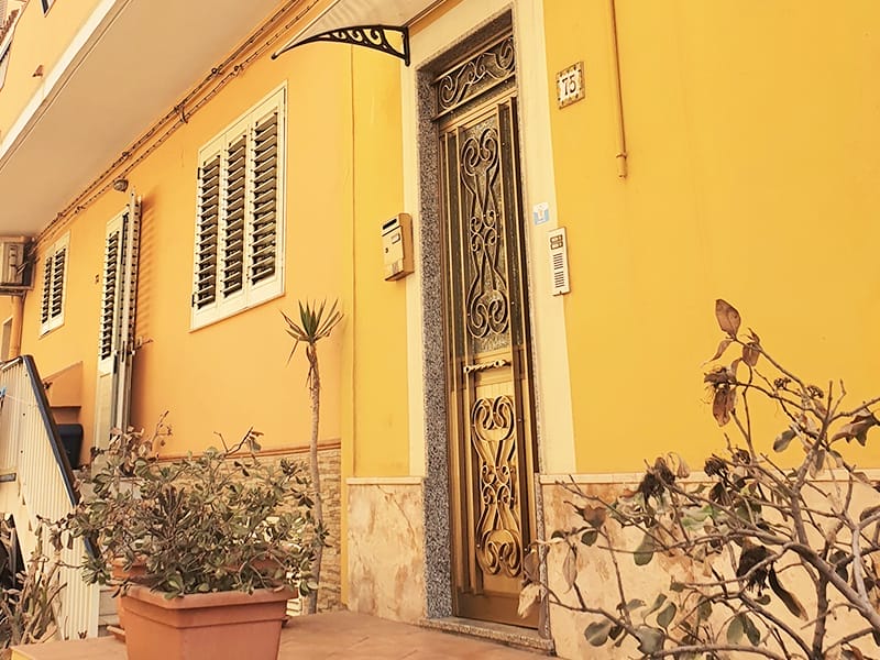 Un edificio giallo con una porta nera, situato a Lampedusa, che offre confortevoli sistemazioni in case vacanze.
