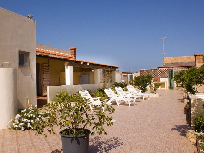 Un patio con sedie bianche e una pianta in vaso, perfetto per godersi la tranquillità di una vacanza a Case Lampedusa.