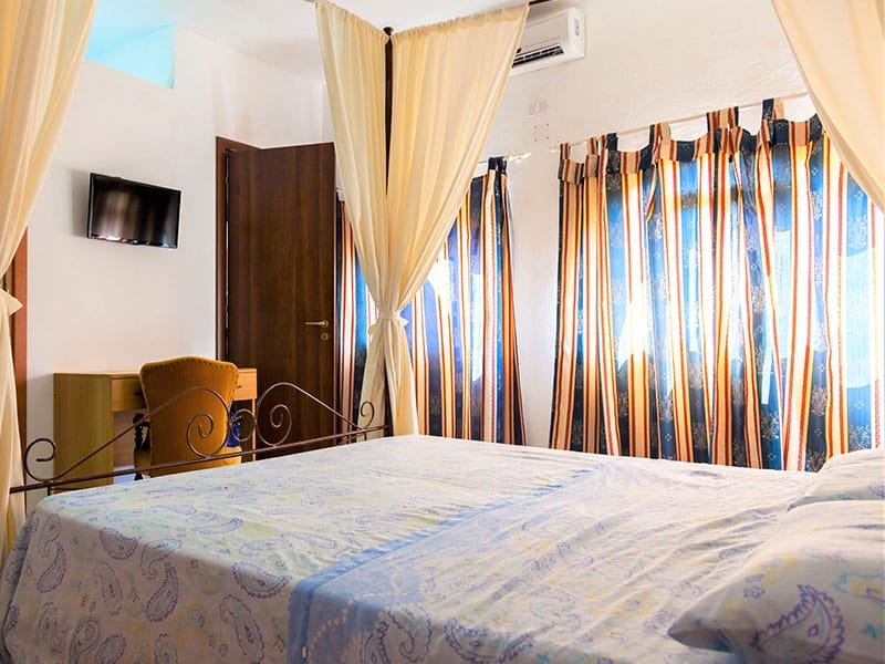 Una casa vacanza a tema Lampedusa dotata di un comodo letto in una spaziosa camera adornata con tende decorative e dotata di una moderna TV.