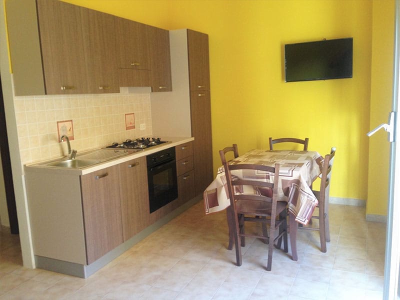 Una cucina con pareti gialle, tavolo e sedie a Case vacanze, Lampedusa.