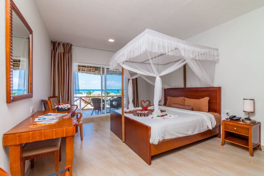 Una camera con letto a baldacchino, tavolo e sedie, dotata di offerta viaggio a Zanzibar alpitour di SBS Viaggi.