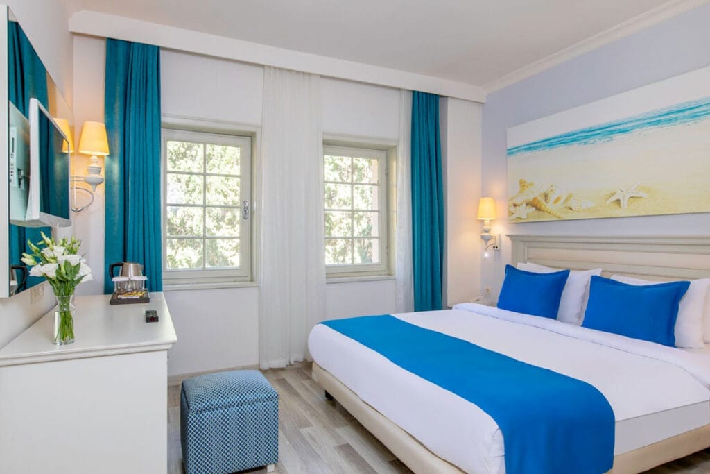 Una camera da letto bianca e blu con un dipinto sul muro. Offerta viaggio a Bodrum in Turchia.