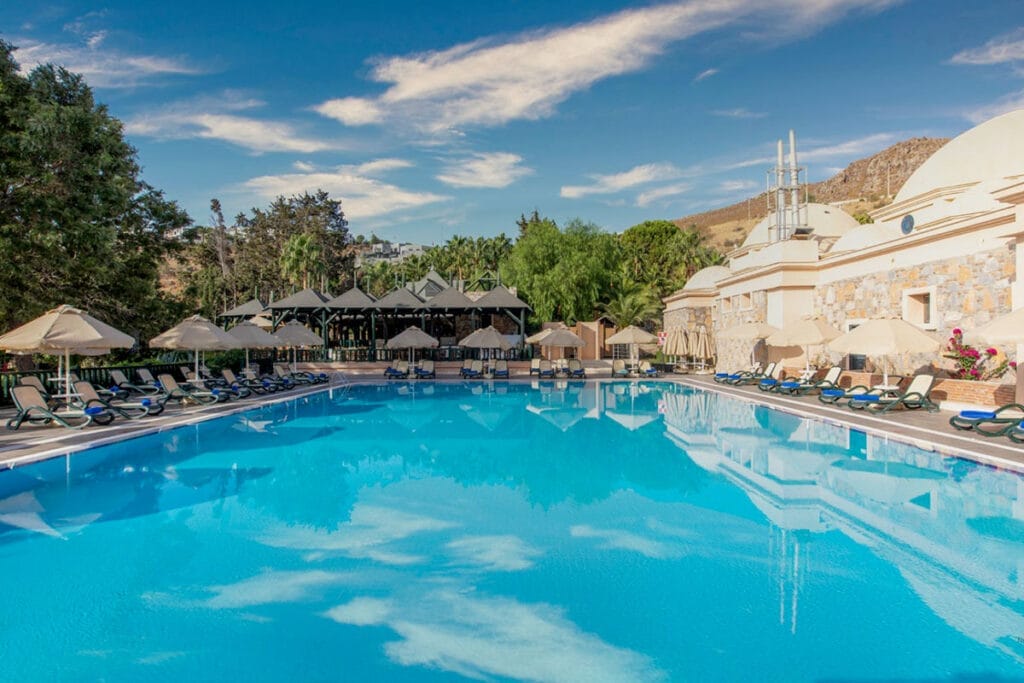 Un'offerta viaggio a Bodrum in Turchia che include una piscina con ombrelloni e sedie.