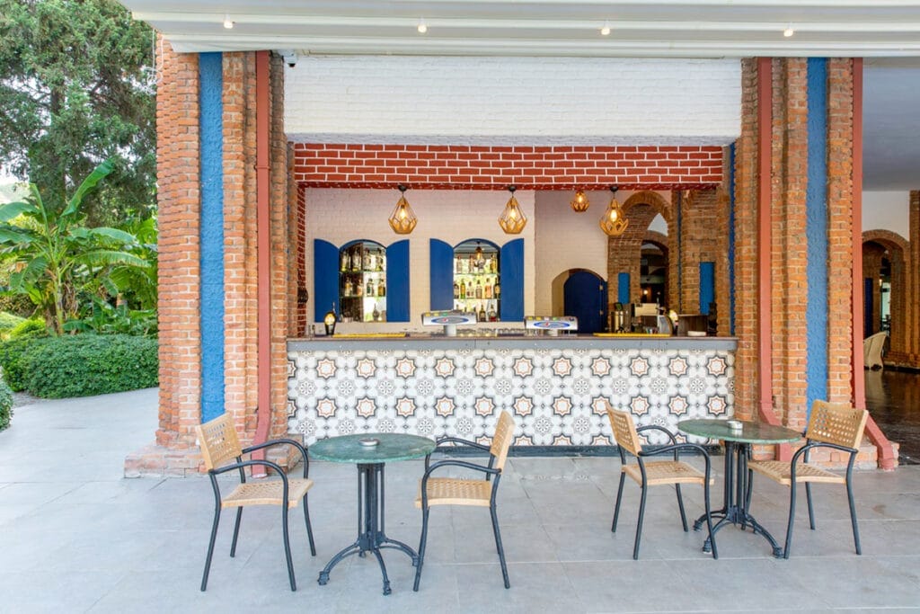 Un bar con tavoli e sedie di fronte a un muro di mattoni offre un ambiente rilassante in cui gli avventori possono godersi i loro drink e conversare.