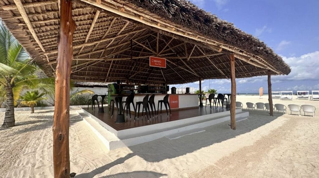 Un bar sulla spiaggia con tetto in paglia situato sulla sabbia, che offre un ambiente rilassante e viste mozzafiato sulla spiaggia Bravo Premium Kendwa.