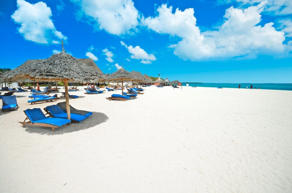 Una spiaggia di sabbia bianca con sedie a sdraio e ombrelloni blu, caratterizzata dalla Bravo Premium Kendwa Beach.
