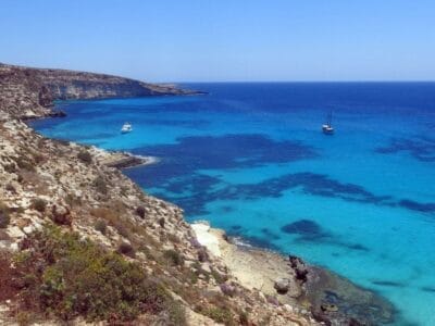 Una scogliera rocciosa che si affaccia su un mare cristallino, regalando panorami indimenticabili agli ospiti che soggiornano al Residence a Lampedusa di SBS Viaggi.