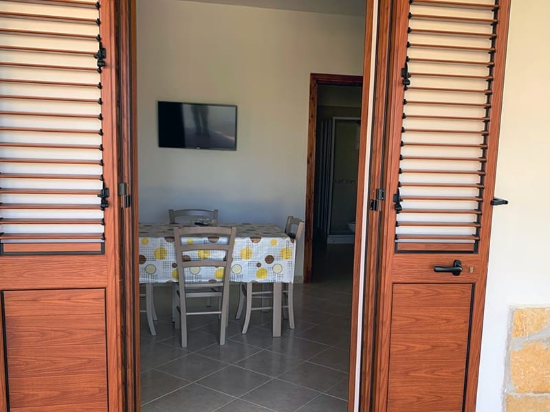 Una porta di legno che conduce in una stanza con tavolo e sedie del Residence a Lampedusa.