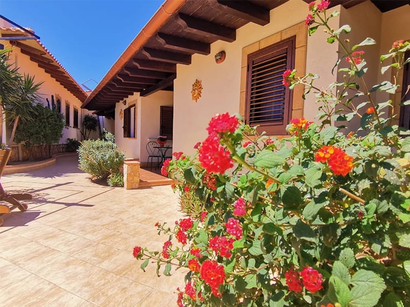 Una villetta caratterizzata da un patio adornato dai vivaci fiori rossi del giardino di Mara Lampedusa.