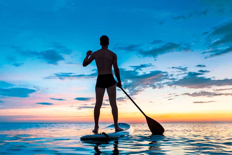 Un uomo in piedi su una tavola da paddle in un pittoresco tramonto vicino al resort.