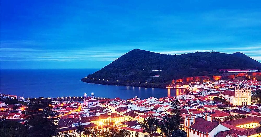 Una città sulle Isole Sao Miguel è illuminata di notte con una montagna sullo sfondo.