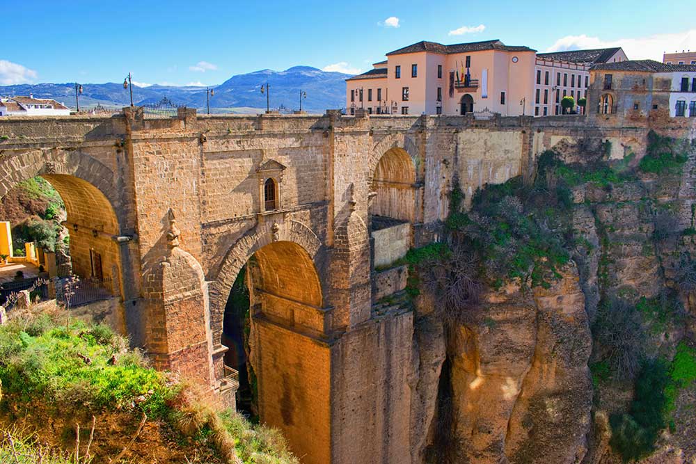 Un pittoresco ponte sospeso su una scogliera, che offre una vista mozzafiato sulla vivace città sottostante. Perfetto per un tour panoramico in Andalusia.