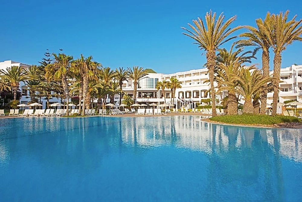 Una piscina di fronte a un hotel con palme a Estensione Mare Agadir.