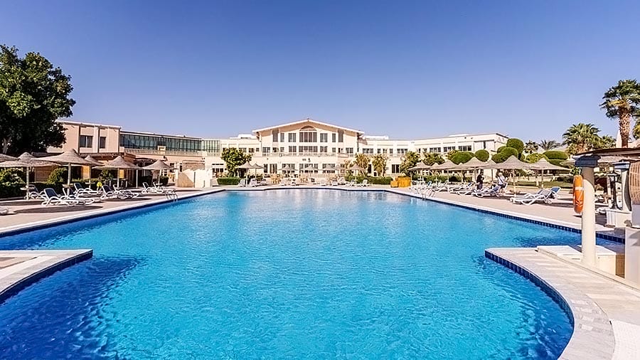 Una grande piscina all'aperto in un resort con lettini sotto un cielo azzurro e limpido, parte di un'offerta viaggio a Marsa Alam.