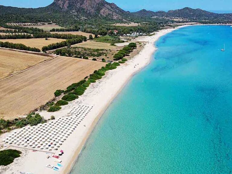 Una veduta aerea di una spiaggia con acqua azzurra e sabbia bianca, perfetta per una vacanza rilassante nel resort Sardegna offerto da SBS Viaggi.