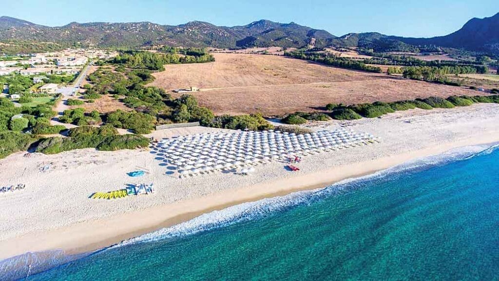 Una veduta aerea di una spiaggia con ombrelloni e sedie a sdraio in un resort in Sardegna.