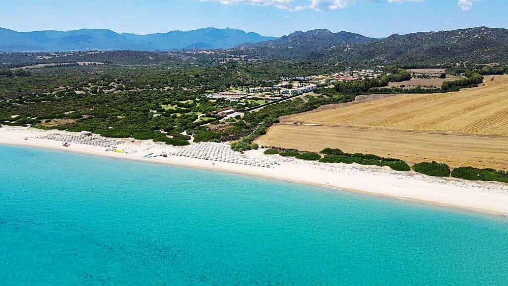 Una veduta aerea di una spiaggia e delle montagne della Sardegna. Offrire un viaggio emozionante con SBS Viaggi.