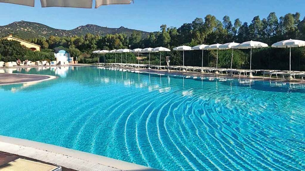 Una piscina con ombrelloni e sdraio attende gli ospiti del resort in Sardegna prenotato tramite SBS Viaggi.