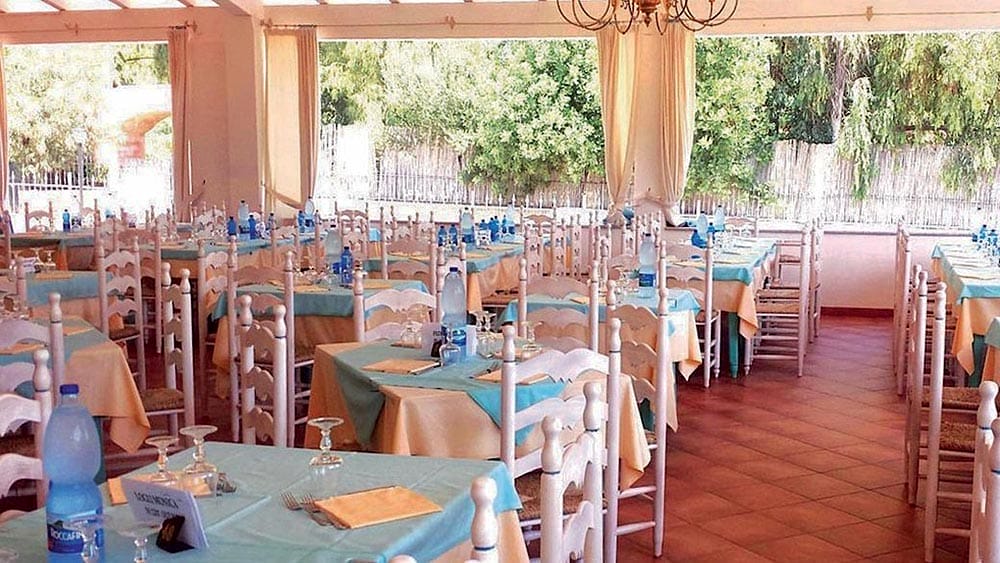 Sala da pranzo allestita per un evento a Marina Torre Navarrese, con tavola e lampadari blu e bianchi.