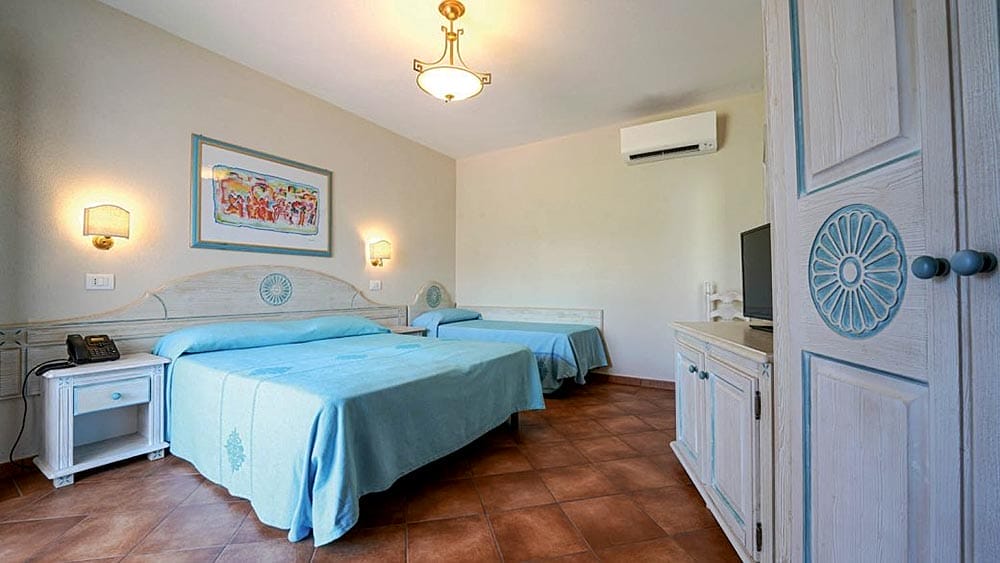 Una camera doppia ordinata con biancheria da letto blu, pavimento in cotto, aria condizionata e arredamento tradizionale di Marina Torre Navarrese.