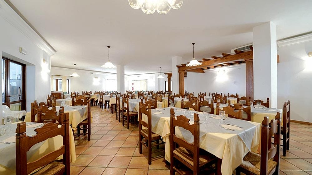Ampia sala da pranzo nel Club Esse Cala Gonone, con sedie in legno e tavoli apparecchiati, pronta per gli ospiti.