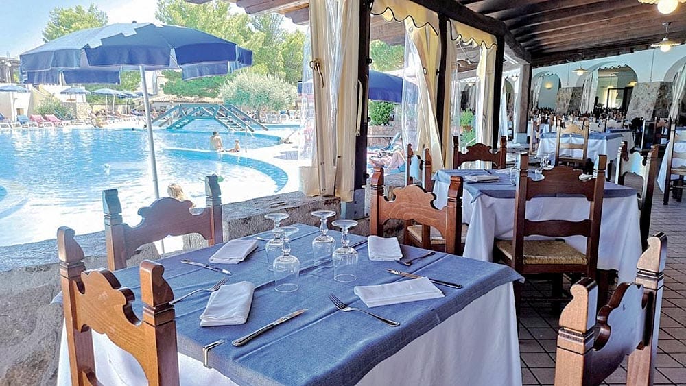 Ristorante all'aperto al Club Esse Cala Gonone con tavoli apparecchiati, affacciato su una piscina in Sardegna.