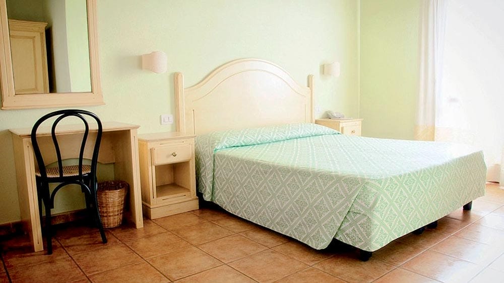 Un letto in una camera del Club Esse Cala Gonone con pareti verdi e mobili bianchi.
