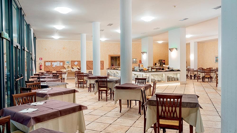 Sala da pranzo spaziosa e vuota con tavoli e colonne apparecchiate presso l'Hotel Club Esse Palmasera, Sardegna.