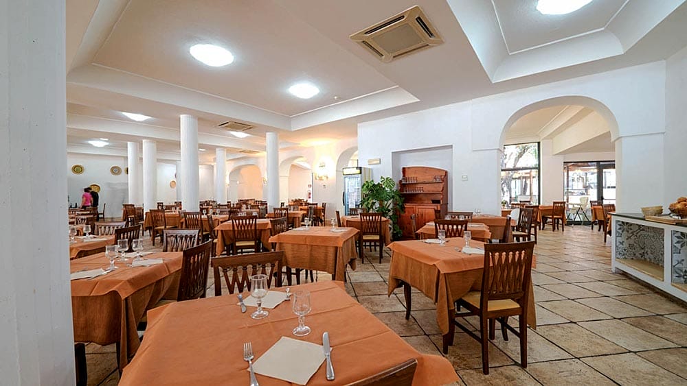 Spaziosa sala da pranzo presso il Club Esse Palmasera Resort, allestita per il servizio, caratterizzata da colonne bianche e archi in Sardegna.