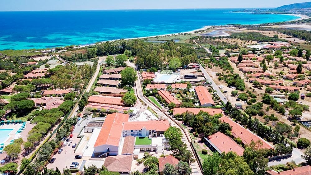 Una località costiera con ville allineate, piscine e la vicina spiaggia di Eurovillage Sardegna.