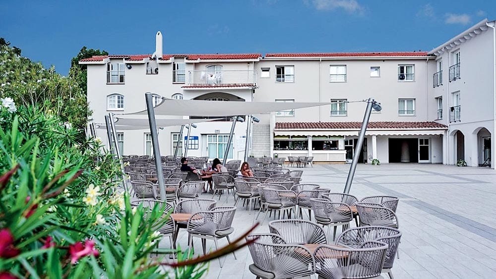 Posti a sedere all'aperto nel patio dell'hotel Eurovillage Sardegna con sedie e tavoli vuoti e un cielo azzurro e limpido.