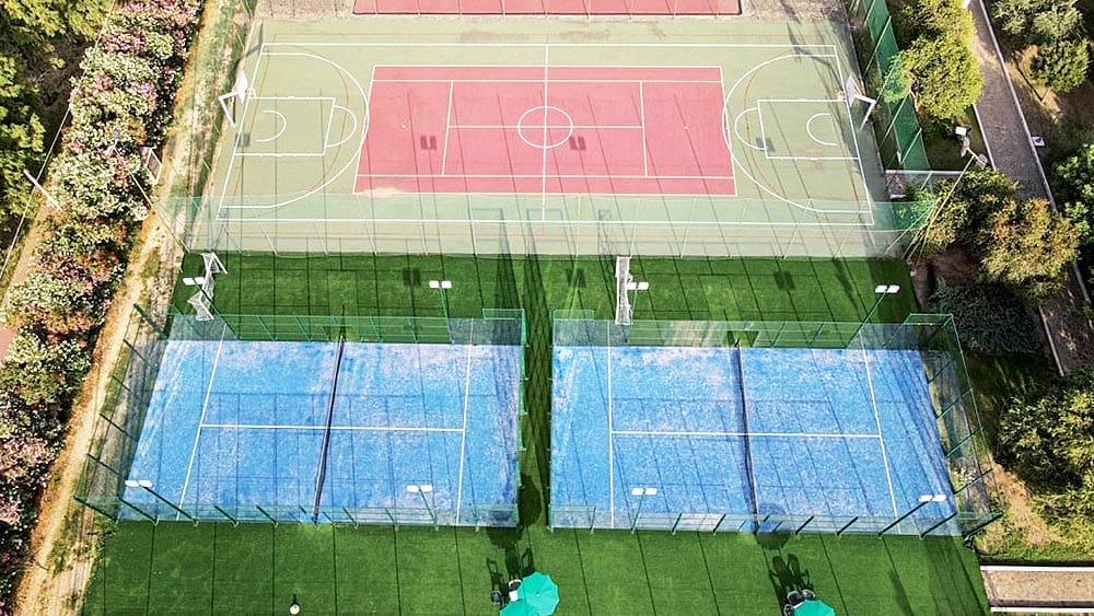 Veduta aerea di un complesso sportivo con campi da tennis, un campo da basket e un giardino.