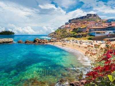 Una pittoresca cittadina balneare della Sardegna, in Italia, con edifici colorati in una giornata soleggiata, caratterizzata da un oceano cristallino e una spiaggia sabbiosa.