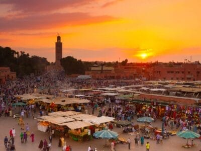 Tramonto su una vivace piazza del mercato in Marocco con folle e bancarelle, con un minareto sullo sfondo.