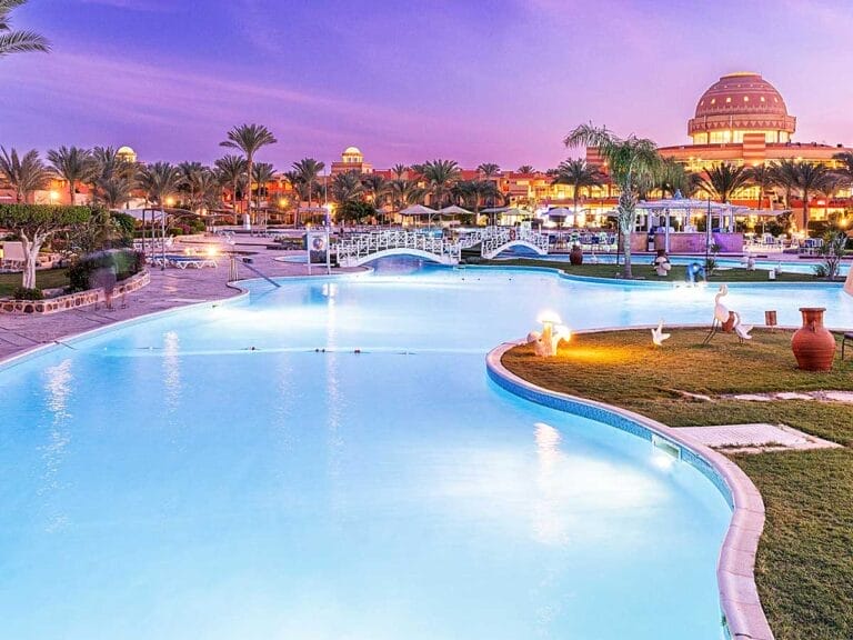 Una tranquilla scena crepuscolare al Malikia Resort Abu Dabbab con una piscina ed edifici illuminati sullo sfondo.