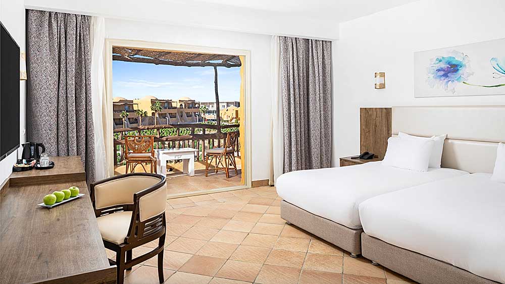 Camera d'hotel con balcone affacciato sul paesaggio urbano, letti gemelli e arredamento contemporaneo. Villaggio Mar Rosso offerta viaggio marsa Alam.
