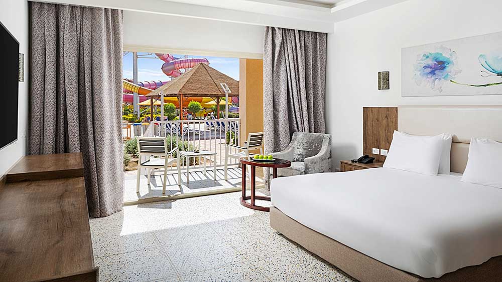 Luminosa camera d'albergo con arredamento moderno e vista sulla piscina all'aperto, parte di un'offerta viaggio Marsa Alam al Villaggio Mar Rosso.