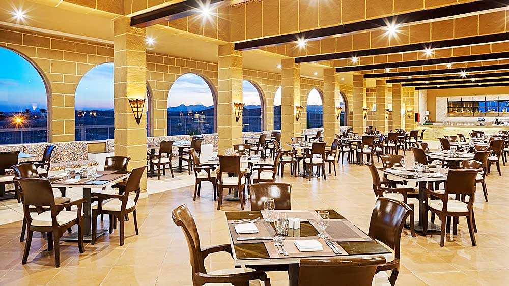 Ampia sala da pranzo con tavoli apparecchiati, archi e vista sulle montagne al tramonto nel Villaggio Mar Rosso.