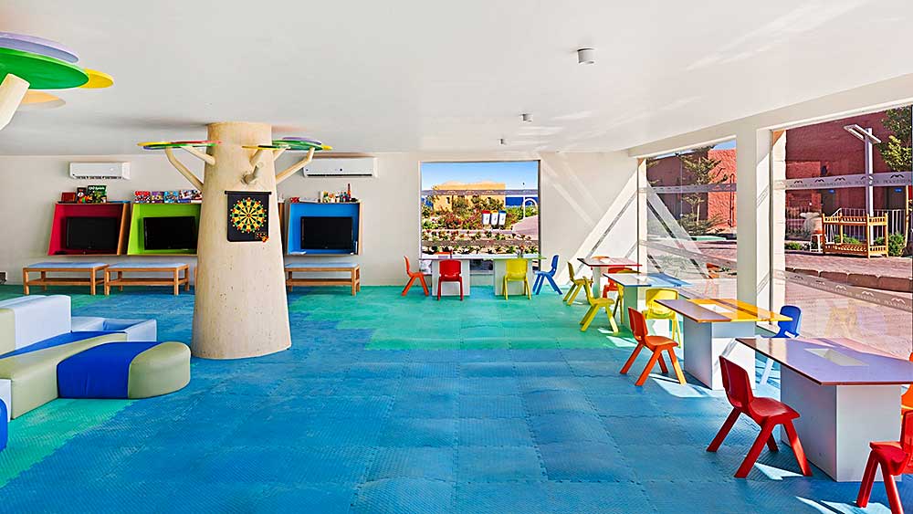 Sala giochi per bambini luminosa e colorata, con varie disposizioni di posti a sedere e giocattoli, che si apre su un'area giochi all'aperto presso il Villaggio Mar Rosso.