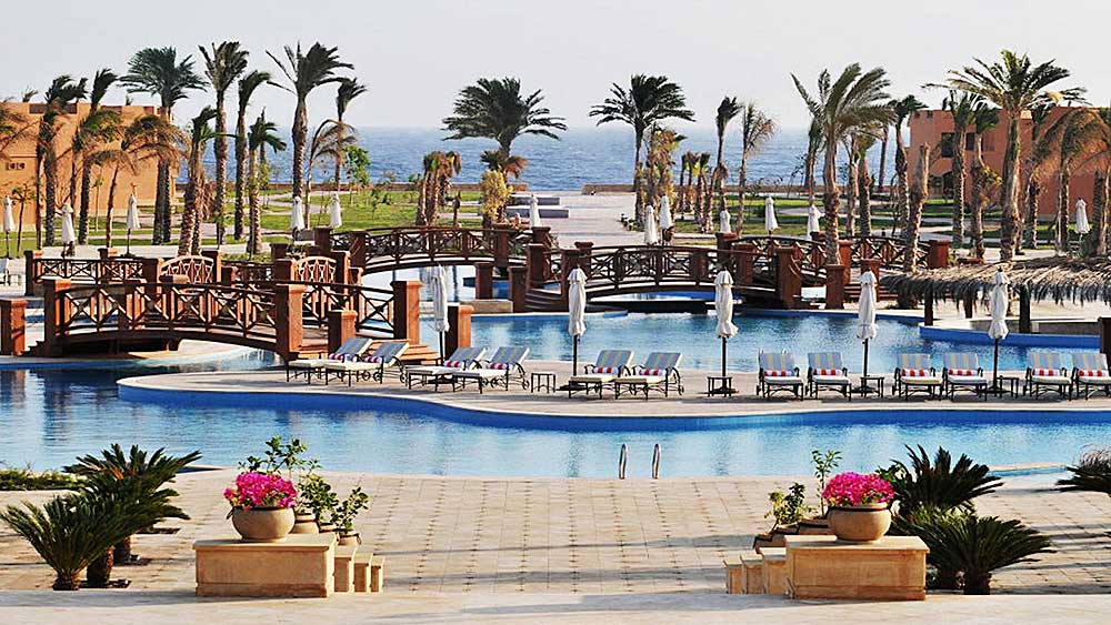 Lussuosa piscina del resort Villaggio Mar Rosso circondata da palme con ponti e sedie a sdraio.