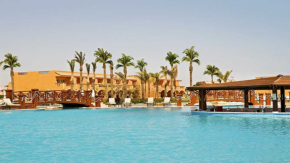 La tranquilla piscina del resort Villaggio Marsa Alam è delimitata da palme e lettini sotto un cielo limpido.