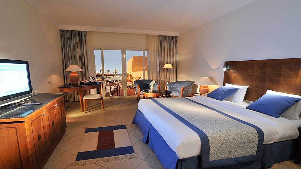 Una camera d'albergo ben arredata al Villaggio Mar Rosso con due letti singoli, una scrivania, una poltrona e un balcone con vista.