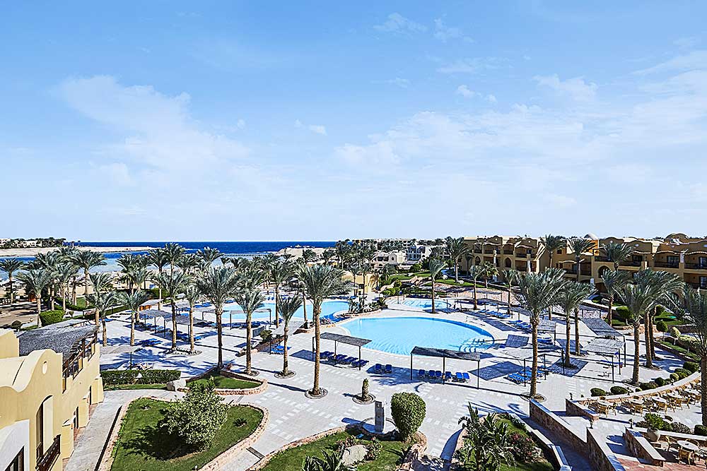 Un resort costiero offerta villaggio Marsa Alam con una grande piscina, palme e sedie a sdraio sotto un cielo azzurro e limpido.