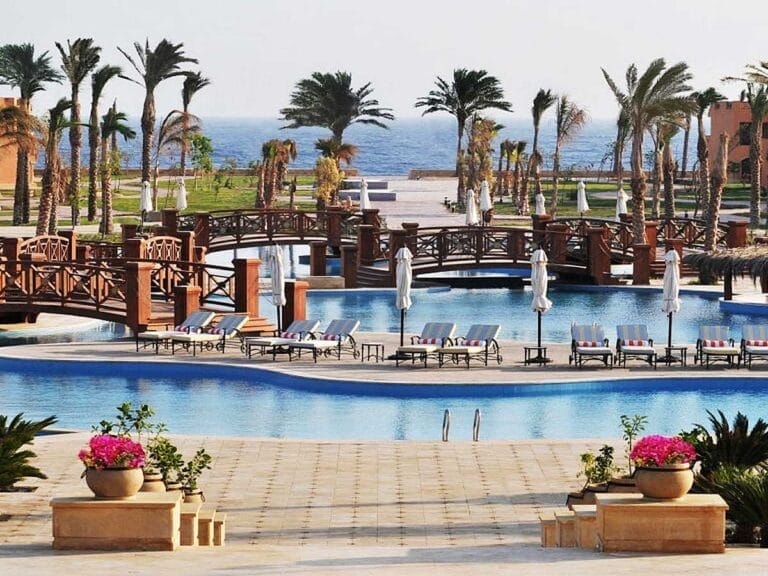 Resort di lusso con piscine, palme e un ponte di legno sotto un cielo limpido - Offerta Villaggio Mar Rosso.