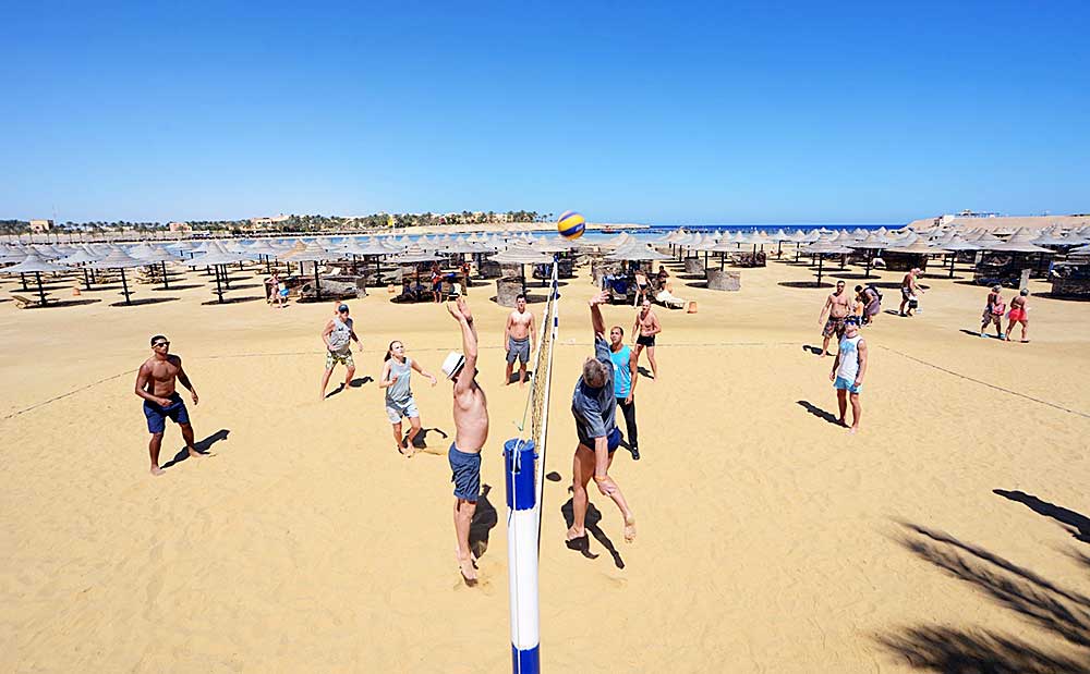 Un gruppo di persone si gode una vivace partita di beach volley sotto un cielo azzurro e limpido, nell'ambito della loro offerta villaggio Marsa Alam.