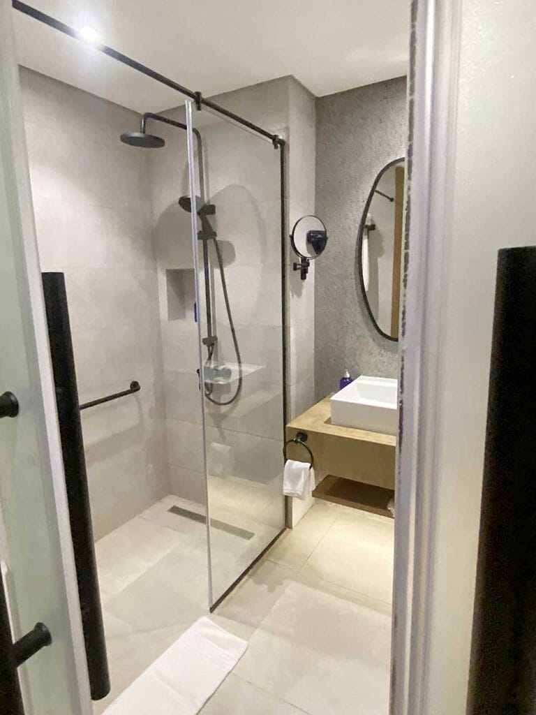 Bagno moderno al Villaggio Sharm El Sheikh con cabina doccia in vetro, lavabo a parete e specchio circolare.